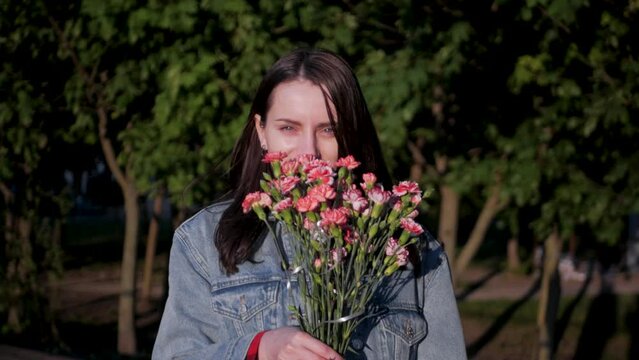 Gorgeous white model smiling and sniffing a bouquet of pink and red flowers. Dreamy beautiful girl with sparkling eyes with flowers received from loved one. Girlfriend inhaling scent of flowers
