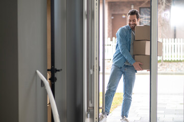 Man holding stack of boxes entering house