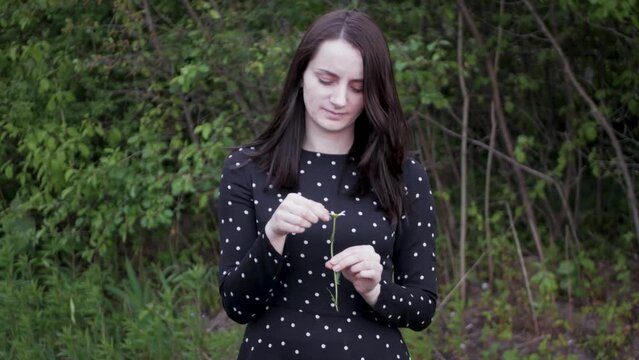 Cute young woman guessing if her loved one loves her back with camomile flower. Concept of he loves me or he loves me not by ripping petals from camomile flower. Happy outcome of predicting future
