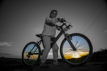 Fototapeta na wymiar Child on a bicycle on a background of green field and with the rays of the evening sun.