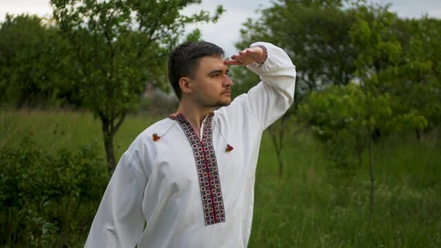 Calm and concentrated caucasian man in traditional embroidered vyshyvanka looking into distance and surveying the horizon. Ukrainian in authentic national shirt scouting the skyline outdoors
