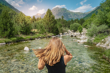 Summer background with a girl with golden blonde hair in front of a crystal clear river and high mountain.