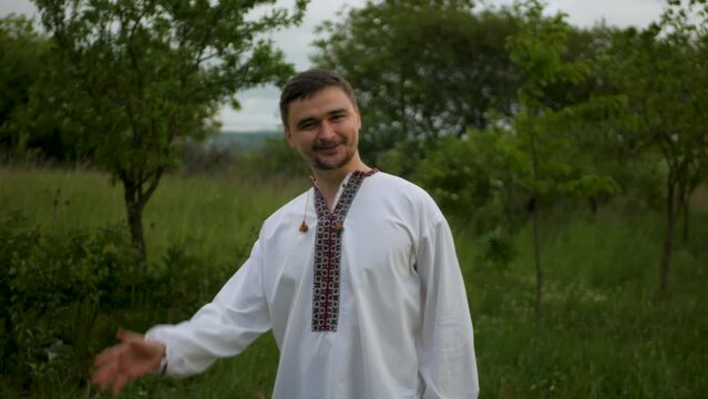 Smiling caucasian man in traditional Eastern European embroidered vyshyvanka turning around and waving hand to viewer. Adult white male in authentic long shirt friendly greeting and waving hello

