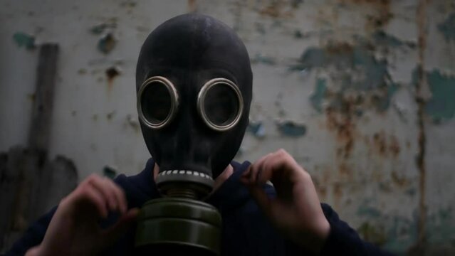 Caucasian man puts on gas mask to protect himself before apocalypse. Adult guy wearing respirator in dark and grim environment. Concept of preparing for chemical and nuclear war with gas helmet
