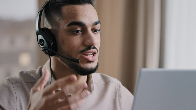 Emotional male operator businessman arab man guy service assistant recruiter wear headphones with microphone speak at webcam laptop provide telephony support give advice online consultation for client