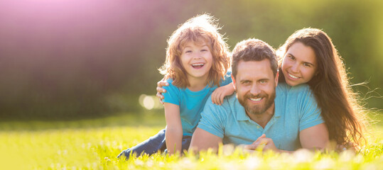 Family of mother dad and son child relax in summer park. Banner of Happy family Lying on grass. Young mother and father with child son play in the park resting together on the green grass.