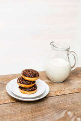 Mini donuts covered with chocolate glaze served with bottle, jug, glass of milk. Stack of tasty sweet sugar creamy or icing doughnuts dessert food on plate and napkin on kitchen. national donuts day