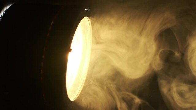 close up view of professional light source yellow color for filming, sunlight in dark room with smoke around. professional fresnel lens is mounted on video light.