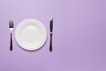 Empty dish with knife and fork on color background, top view