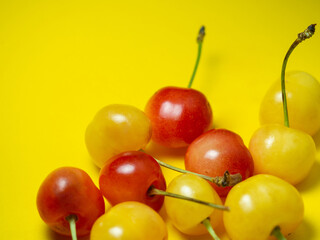 Sweet cherry with a stem on a yellow background. Bright table. Natural berries on the table.  Delicious food. Berries of different colors.