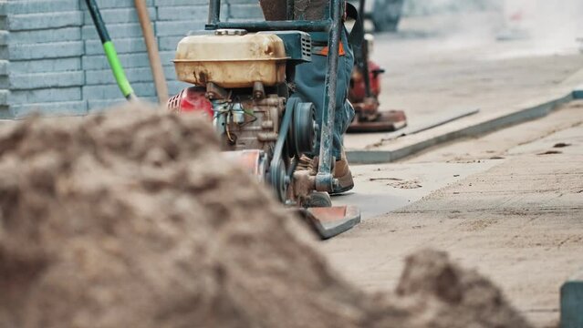 Roadworks Construction Worker Using Ground Plate Compactor Preparing Surface for Laying Sidewalk Pavement Flagstones