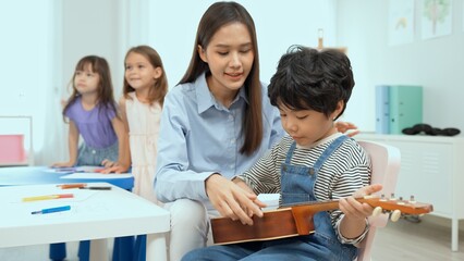 Young asian teacher teaching guitar and ukulele to his little boy.Little boy learning guitar at kindergarten.Close up,Ukulele class at school. Child learning guitar from her teacher.Musical education.