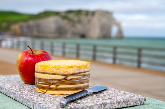 Tasting of yellow livarot cow cheese from Calvados region served with apple and view on alebaster cliffs Porte d'Aval in Etretat, Normandy, France