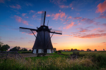 Fototapeta na wymiar Windmills in the Netherlands. Historic buildings. Agriculture. Summer landscape during sunset. Bright sky and the silhouette of a windmill. Photography for design.