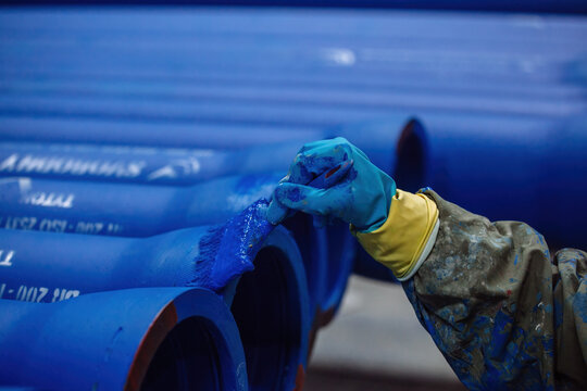 Worker painting new cast iron pipes in blue color