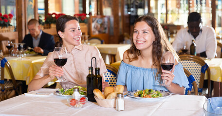 Two cheerful women friends enjoying evening meal in restaurant