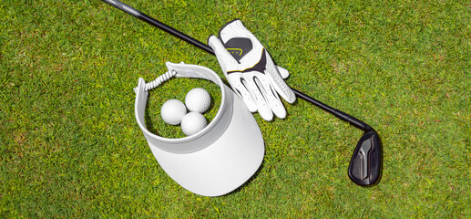 Top view of golf equipment on green grass on a golf course. Flat lay of golf club, balls, glove and cap