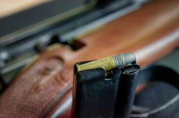 Close up of a clip holding .22 caliber rifle rounds.  Brass and lead bullets in a clip.  Clip in focus with rifle and scope blurred in the background.  - obrazy, fototapety, plakaty