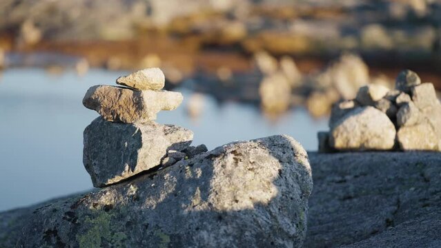 A close-up shot of the small stone cairns on the top of the big boulder. A small pond in the background. Slow-motion, pan right.