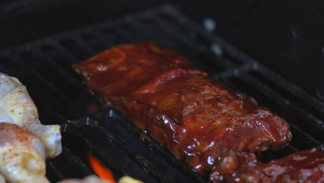 This close up, delicious video shows grill flames rising around bbq ribs on an outdoor grill in slow motion.