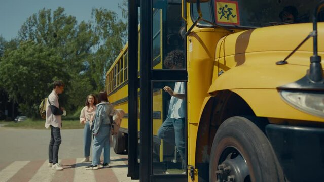 Two school children going out schoolbus. Teenagers standing at bus talking.