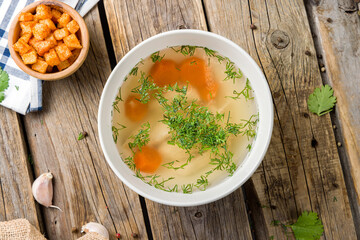 Chicken soup bouillon on a bowl top view on wooden table