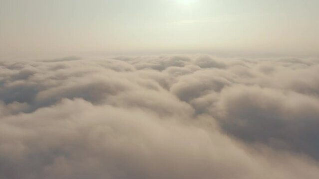 Dolly Out drone shot. Sunset at high altitude above the fog. Cloud motion against background of the sun and sky. Cockpit view: fluffy cumulus clouds and sun - Sun above the clouds.