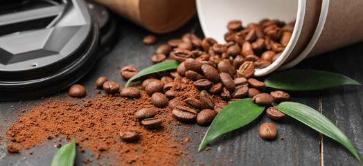 Paper cups, scattered coffee beans and powder on wooden table, closeup
