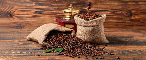 Bags with coffee beans and grinder on wooden background