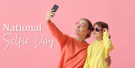 Young woman and her little daughter taking selfie on pink background