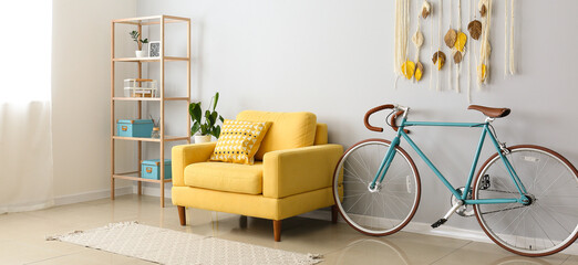 Interior of light living room with yellow armchair, shelf unit and bicycle