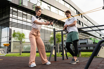 Young couple caucasian man and woman boyfriend and girlfriend or husband and wife training at outdoor open gym instructor giving exercise advice during elastic resistance band tubes workout copy space