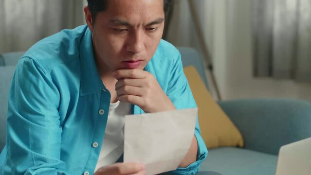 Close Up Of Asian Man Looking At The Bill And Thinking Before Working With A Laptop At Home
