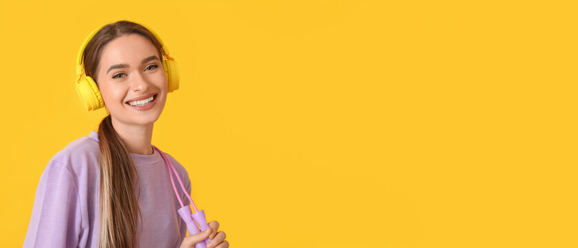 Sporty young woman with jumping rope listening to music on yellow background with space for text