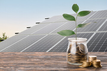 Jar with coins on table near modern solar panels outdoors