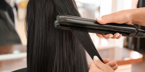 Hairdresser straightening woman's long hair in salon