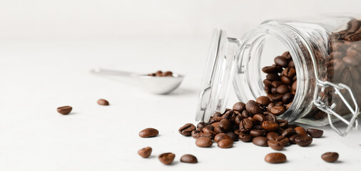 Overturned jar of coffee beans on light background with space for text