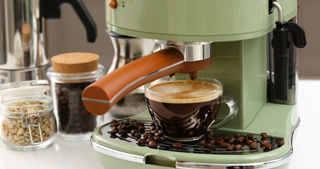 Modern machine with cup of fresh coffee on table in kitchen, closeup