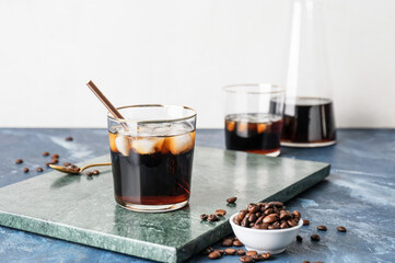 Glass of cold brew with straw and coffee beans on color table against white background