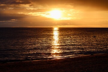 Sunset over calm Baltic sea, in Saulkrasti, Latvia. Sun shining from behind clouds and bright reflection on water. Selective focus