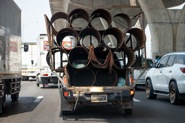 A fully loaded pickup truck carries steel pipes on the highway