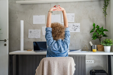 One woman adult mature caucasian female at her office desk sitting at work stretching arms...