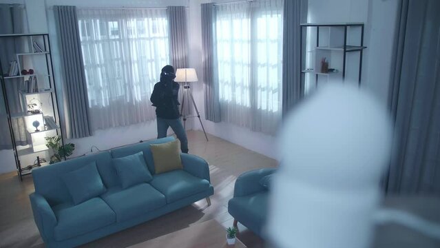 Thief man with flashlight puts the black Fabric covering closed circuit television camera while walking in someone's house
