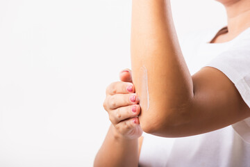 Closeup young Asian woman applies lotion cream on her elbow, studio shot isolated on white...