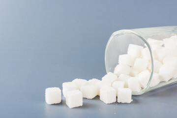 White sugar cube sweet food ingredient spilled out of the glass, studio shot isolated on a gray...