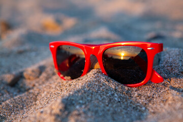 sunglasses on the beach, reflection of sunset in the lens 