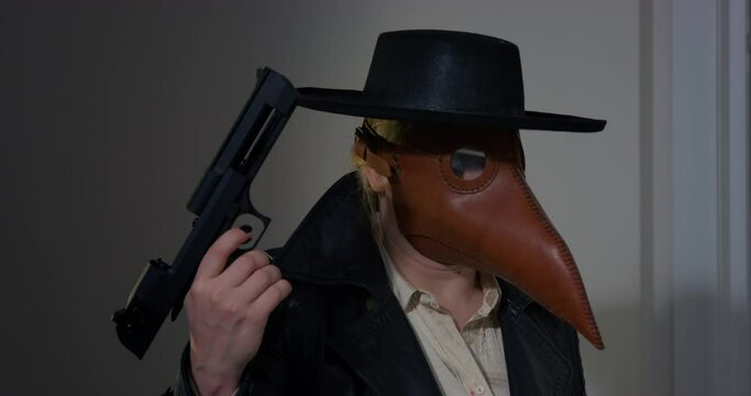 Young woman in plague doctor costume and pointy leather mask inspects room and pulls trigger. Criminal looks around room walking with gun closeup