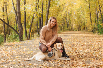 A young woman walking with her beloved labrador dog in autumn park.