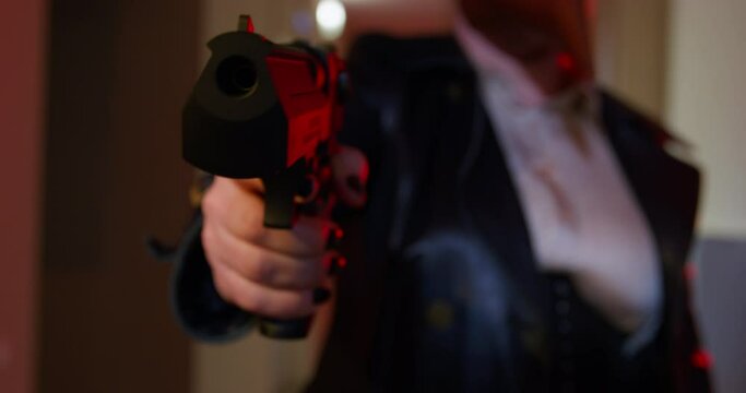 Criminal woman in plague doctor mask and black clothes points gun shooting victim in corridor. Serial killer uses dangerous weapon to attack enemy close view