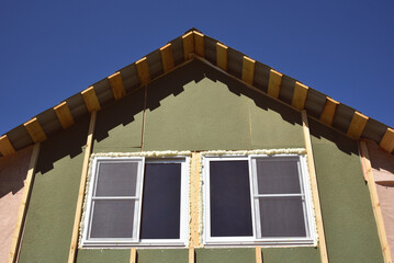 Wall covering of the frame house with panels of vinyl siding. construction or reconstruction, repair of the house. Installation of plastic Windows in a new residential building on blue sky background. - obrazy, fototapety, plakaty